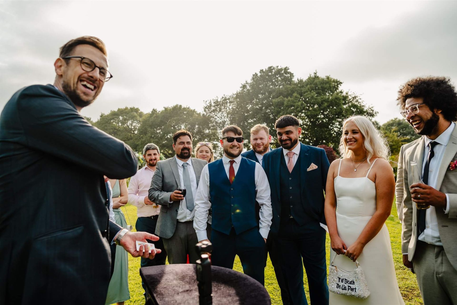 Magician performing a card trick for the bride and guests on the lawn at a wedding drinks reception